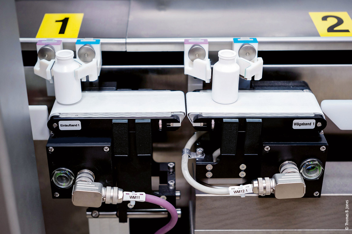 Transfer of containers from XTS to one of two checkweighing systems for inline fill quantity control